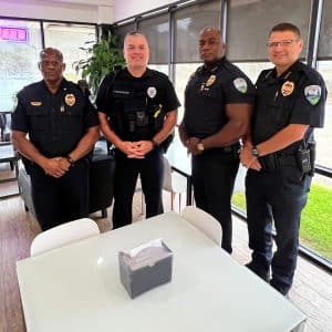 Four uniformed officers standing together inside a community space, encouraging others to join the Alexandria Police Department through service and leadership.